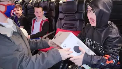 Young man holding a Playstation 5 VR Headset inside our gametruck rental with all his friends and family cheering for him. This gift is included in our premium game truck packages