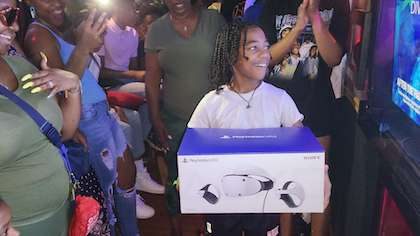Young man holding a Playstation 5 VR Headset inside our gametruck rental with all his friends and family cheering for him. This gift is included in our premium game truck packages